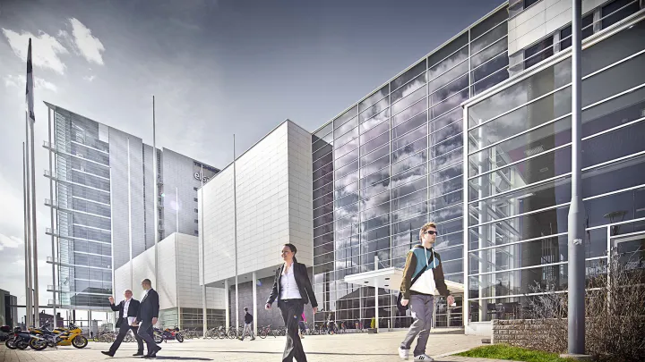 In front of glass-walled building there´s people walking in the sunshine