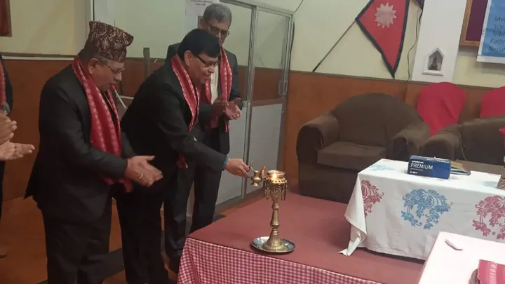 Professor and two other men standing in front of a room having a ceremony. Nepal flag on the wall. 