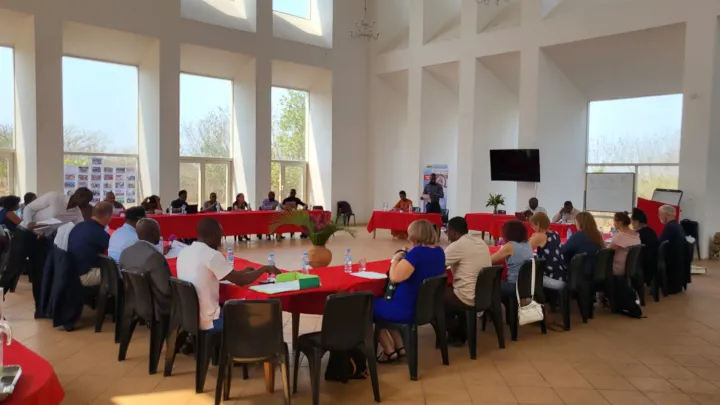 A large group of people sitting by long desks at a conference room.