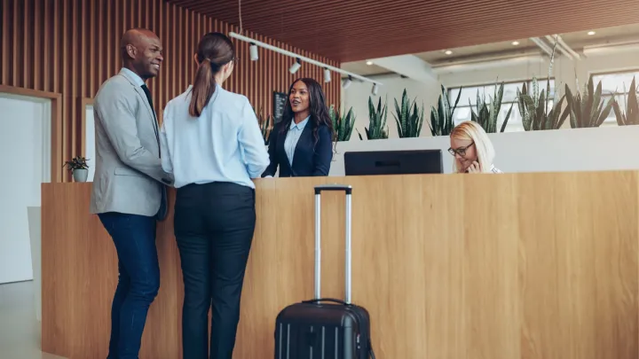 Two smiling guests checking in at a hotel reception.