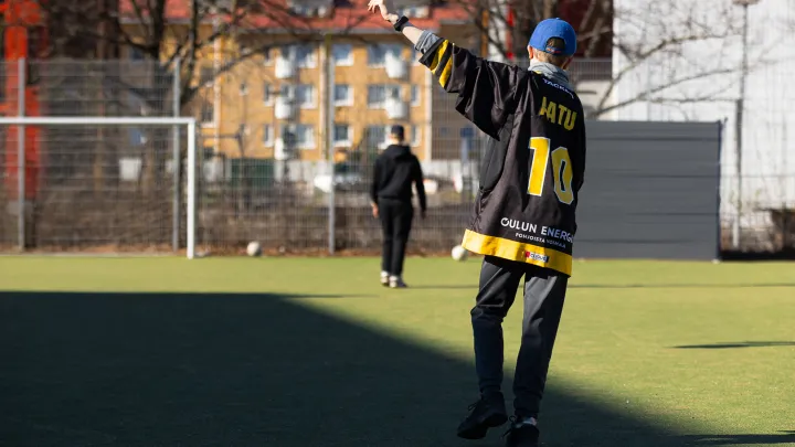 Henkilö pelaamassa jalkapalloa selin kameraan. Hänen vasen kätensä on nostettu ylös ja siinä on liikemittari.